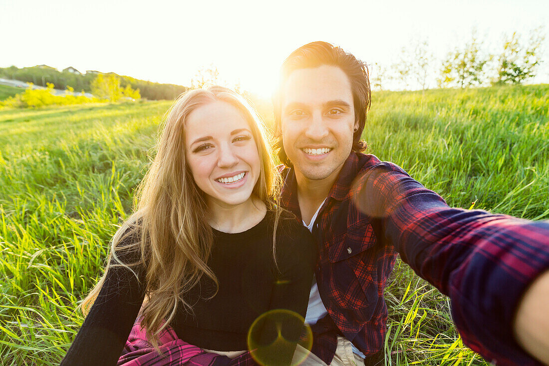 Young couple in a park posing for a self-portrait with their cell phone; Edmonton, Alberta, Canada