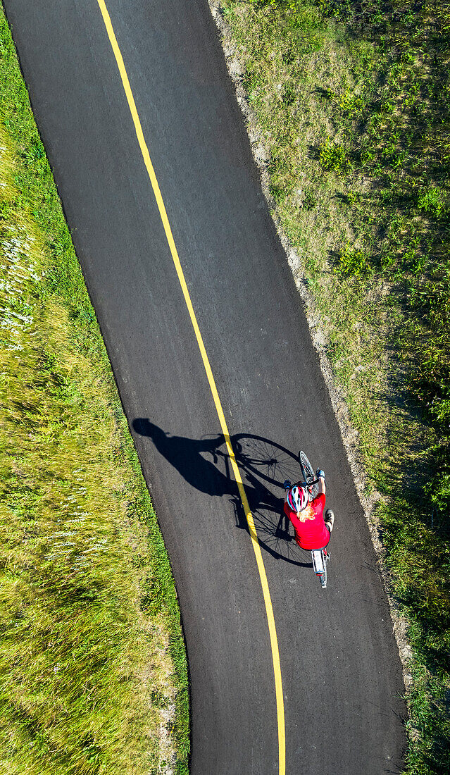 View from directly above a cyclist in a red shirt on a paved cycling trail; Calgary, Alberta, Canada