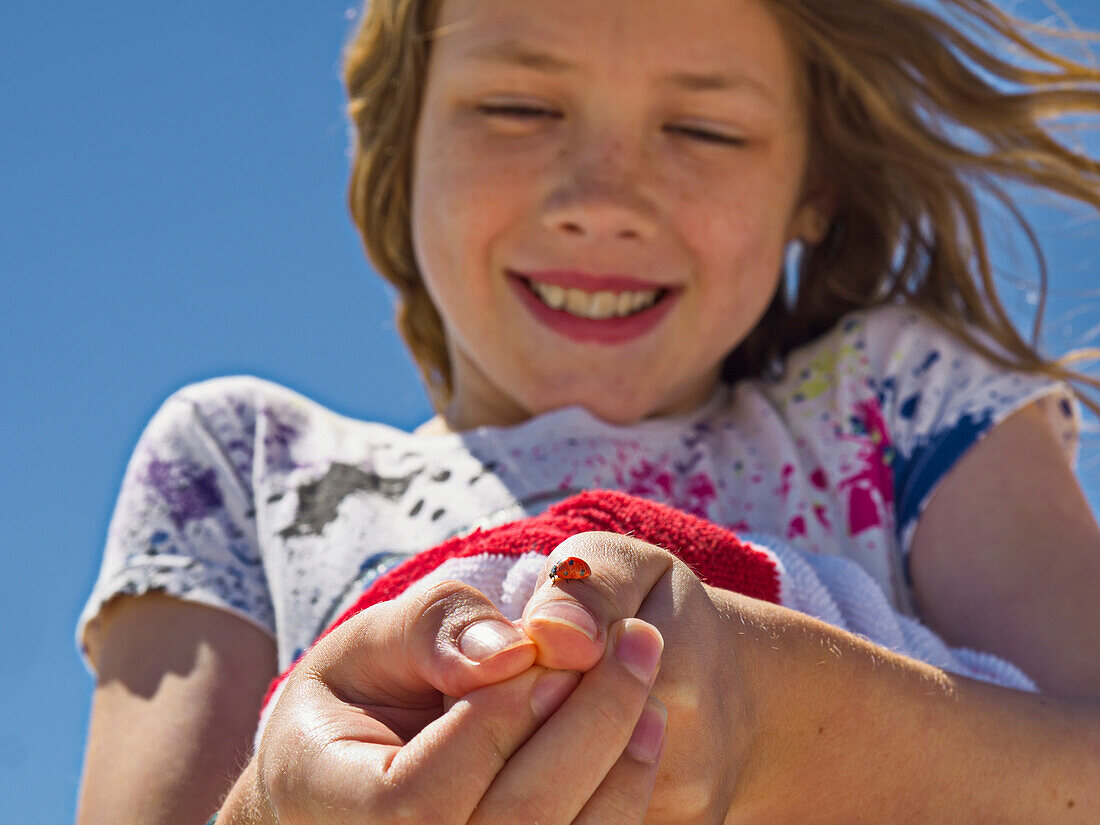 A young girl shows off a ladybug (Coccinellidae) she caught and is holding on her thumb; Destin, Florida, United States of America