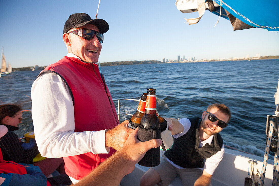People doing celebratory toast with beer on sailboat, Perth, Western Australia, Australia