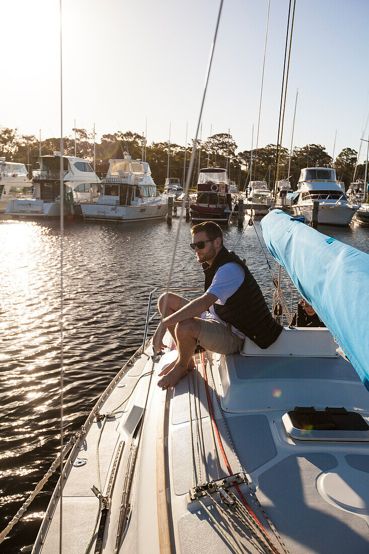 Sailor sitting on foredeck of sailboat, Perth, Western Australia, Australia