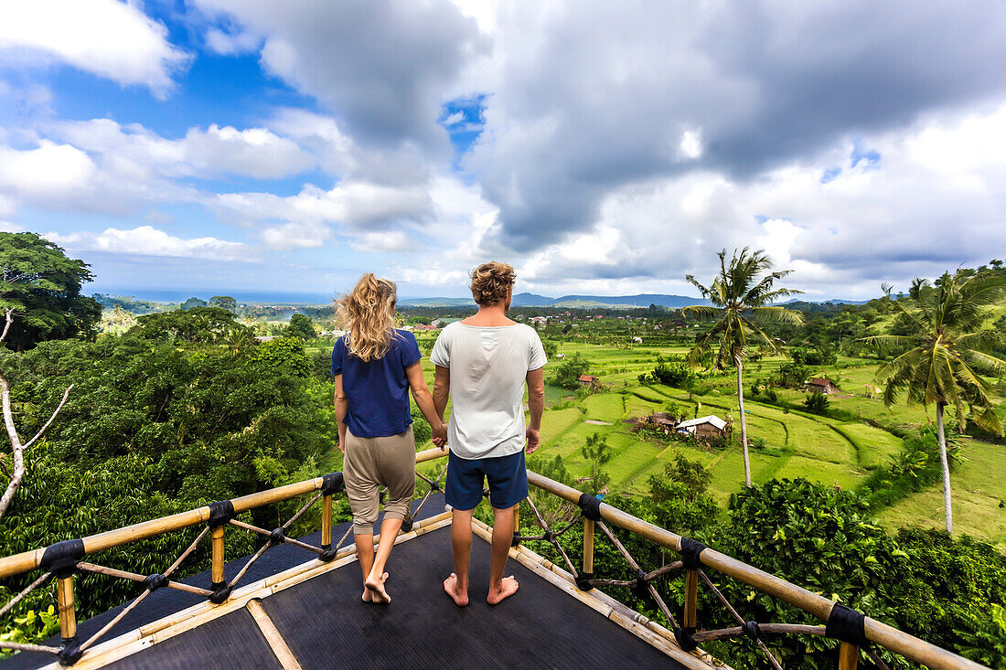 Adult couple standing on tree house balcony and holding hands while admiring landscape, Bali, Indonesia