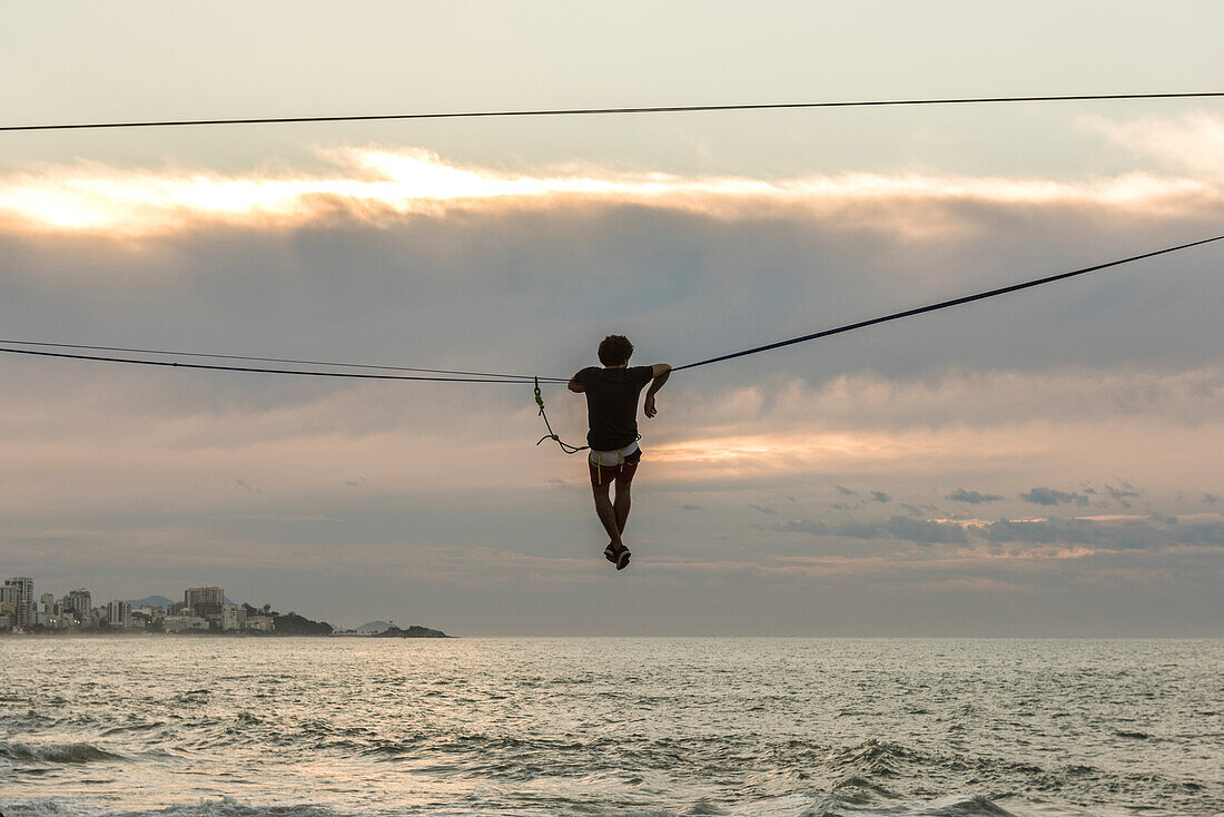 Rear view of man slacklining and waterlining during sunrise in Leblon Beach, Rio de Janeiro, Brazil