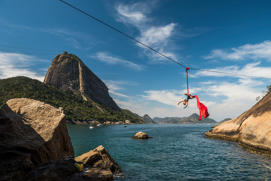 Woman doing aerial acrobatics hanging from highline next to Sugar Loaf Mountain in Rio de Janeiro, Brazil