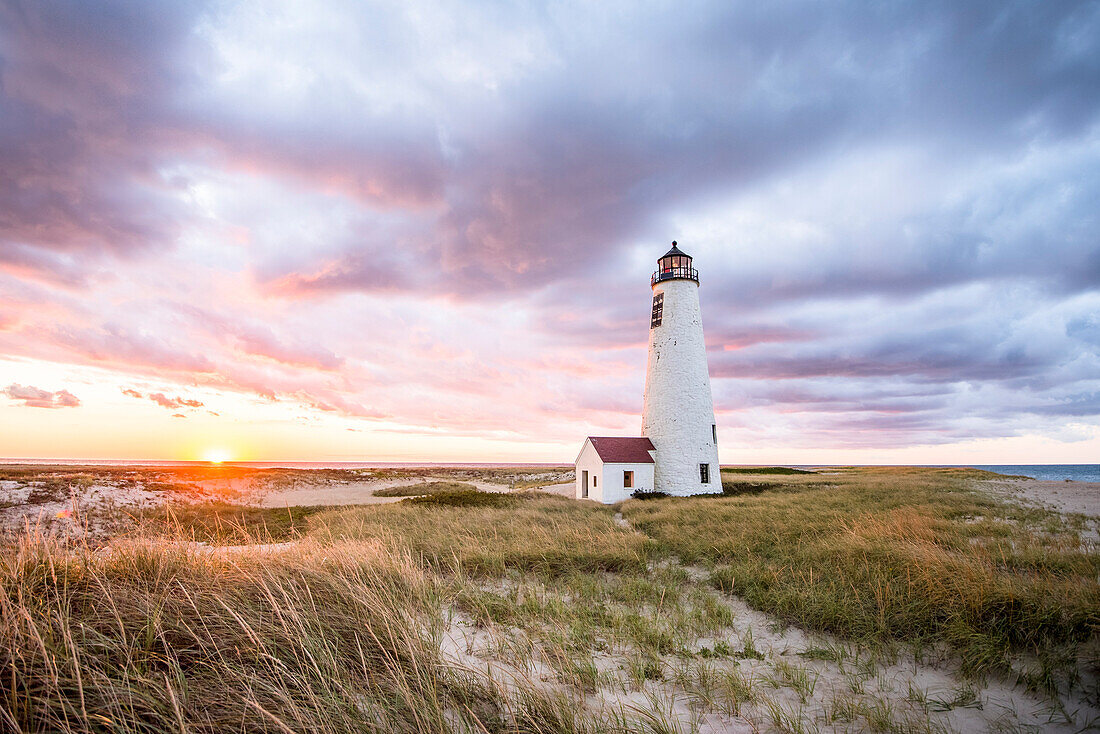 A vibrant colorful sunset of Nantucket's iconic Great Point Lighthouse, isolated on a stretch of sand 7 miles long in the Atlantic Ocean