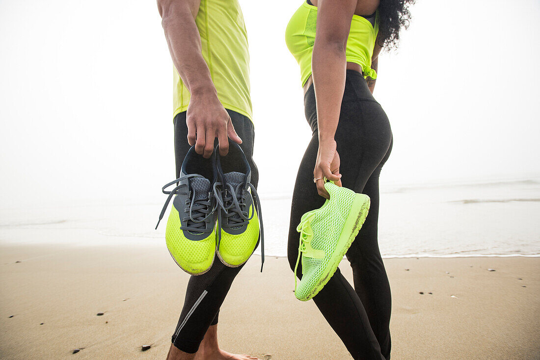 Man and woman standing on coastal beach and holding shoes, Hampton, New Hampshire, USA