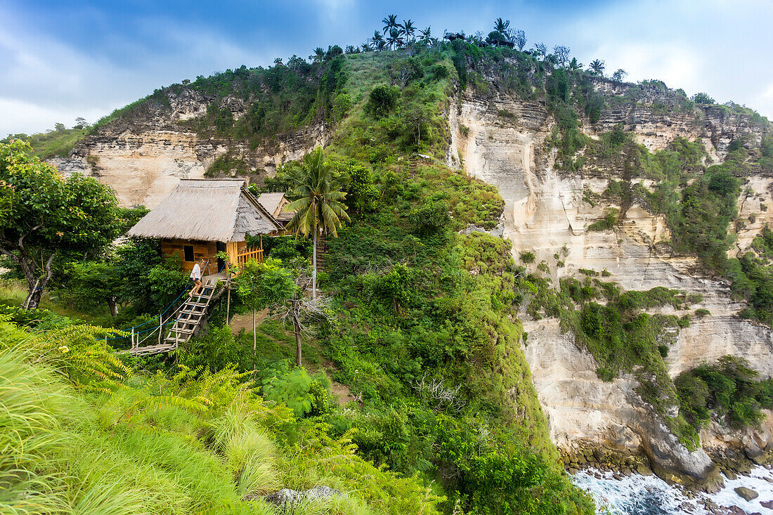 Woman outside thatched roof hut on coast with cliffs, Nusa Penida, Bali, Indonesia