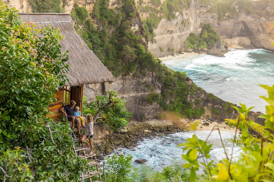 Family on vacations outside thatched roof hut on coastline, Nusa Penida, Bali, Indonesia