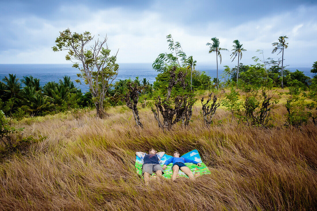 Couple lying on blanket in meadow near ocean coastline, Nusa Penida, Bali, Indonesia