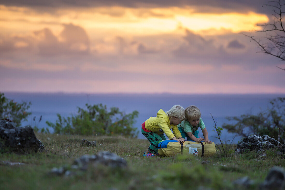 Two boys playing with tent bag at sunset, Nusa Penida, Bali, Indonesia