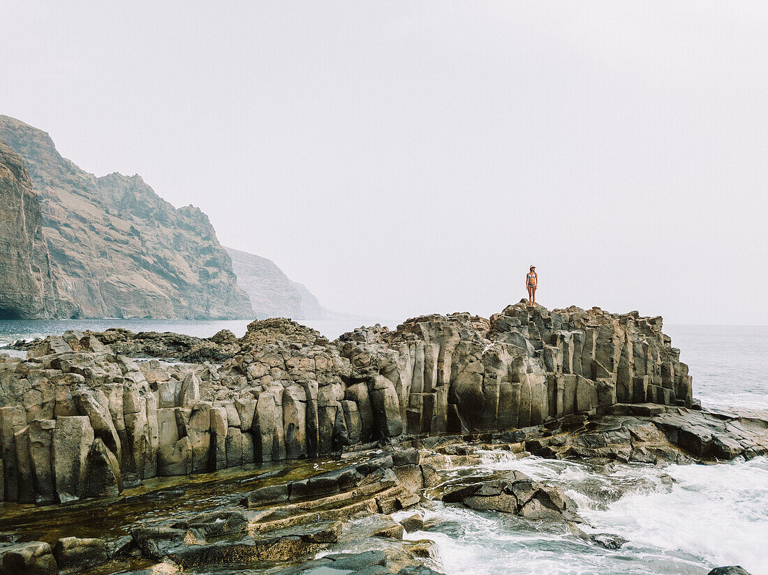 Woman in bikini standing on rocky coastline, Tenerife, Canary Islands, Spain