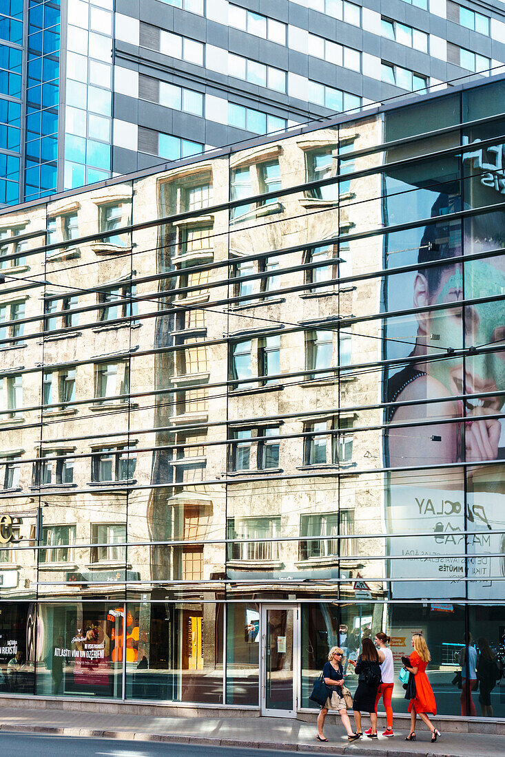 Building reflections with women in brightly coloured dresses on sidewalk near Galeria Riga, Riga, Latvia, Europe