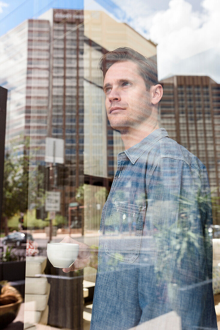 Pensive Caucasian man drinking coffee near window in city