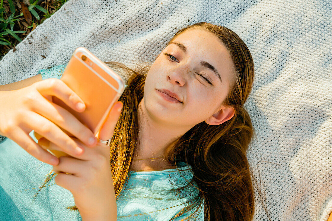 Confused Caucasian girl laying on blanket texting on cell phone