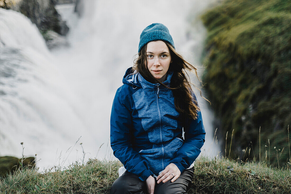 Portrait of serious Caucasian woman sitting near waterfall