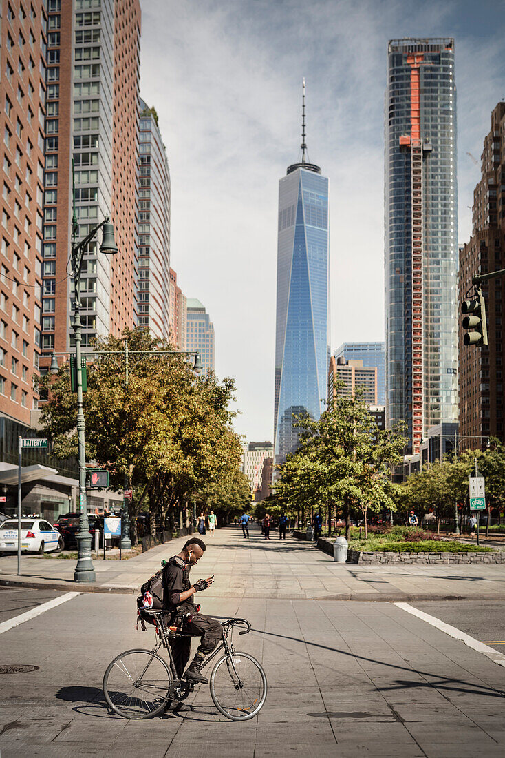 stylischer New Yorker mit Irokese sitzt auf Rennrad vor dem ONE World Trade Center und blickt auf sein Mobiltelefon, Manhattan, New York City, Vereinigte Staaten von Amerika, USA, Nordamerika