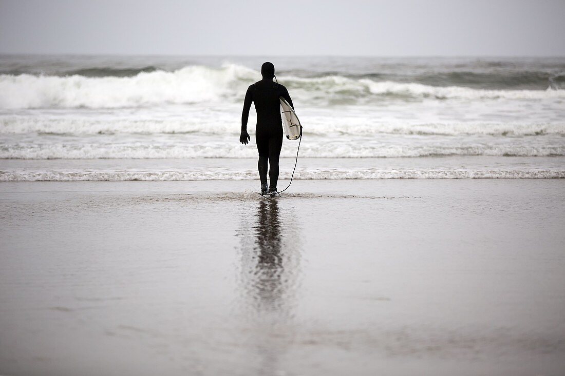 A lone surfer wearing a wet suit prepares to enter Pacific Ocean on Indian Beach along the Oregon Coast.