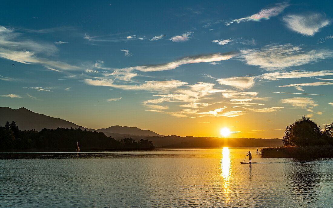 Sonnenuntergang am Staffelsee mit Stehpaddler und Segelboot, Seehausen, Oberbayern, Deutschland