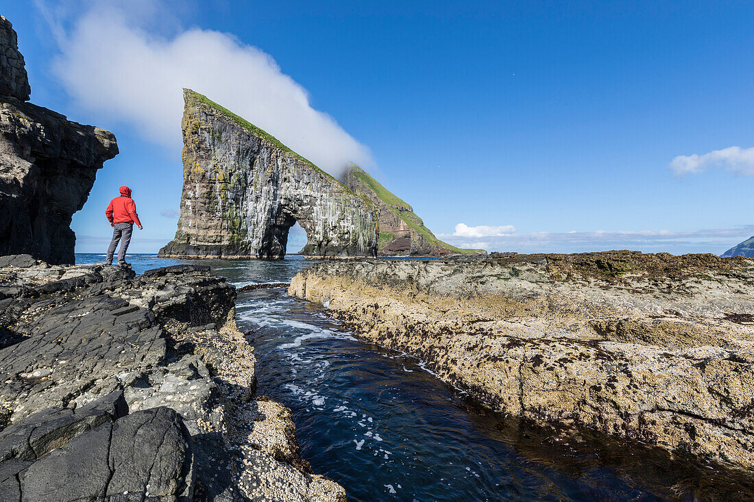 Man on cliffs looks towards the natural arch of Drangarnir rock, Vagar Island, Faroe Islands, Denmark, Europe