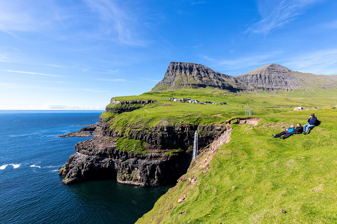 People admire the ocean from green meadows on cliffs, Gasadalur, Vagar Island, Faroe Islands, Denmark, Europe