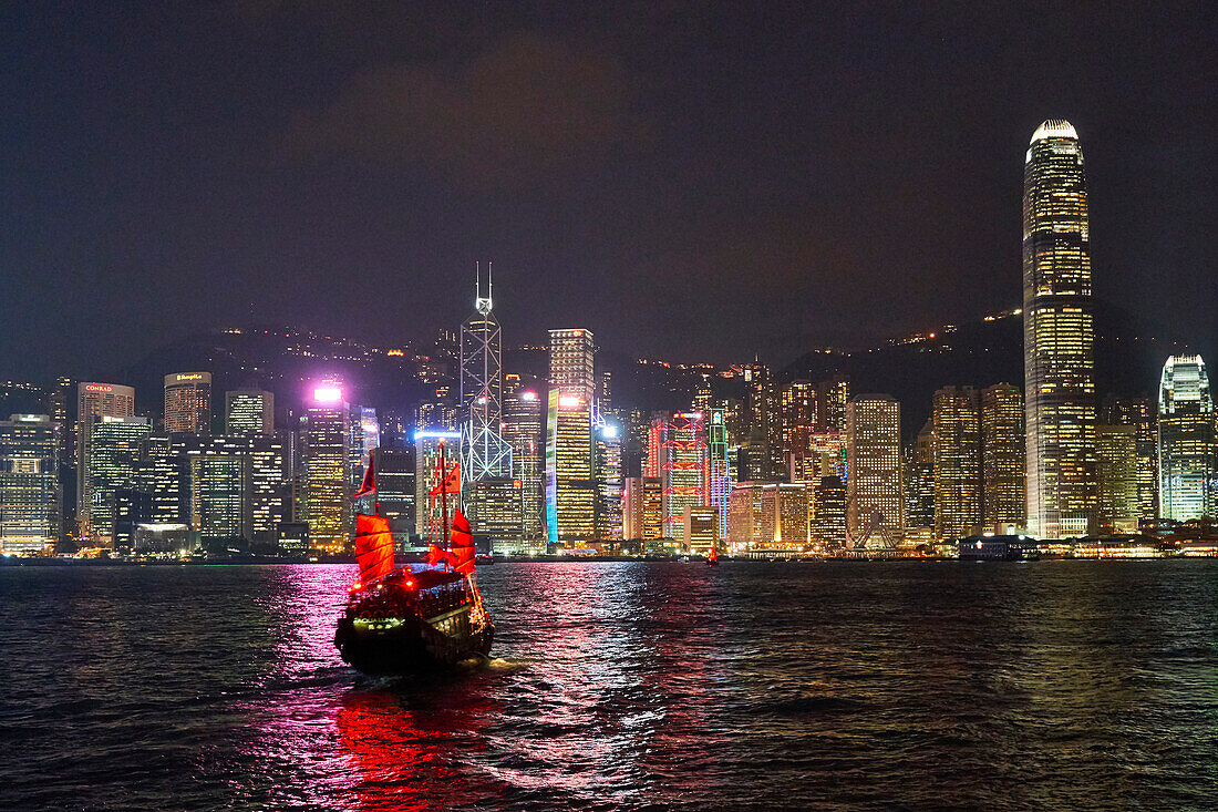 Traditional junk boat on Victoria Harbour with city skyline behind illuminated at night, Hong Kong, China, Asia
