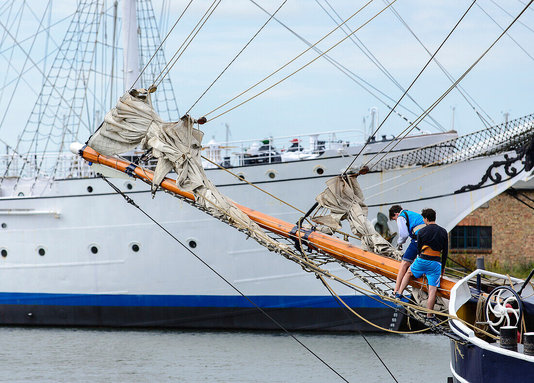 Junge Männer klettern an einem alten Holzsegelschiff. Museumsschiff Gorch Fock 1 ist im Hintergrund zu sehen, Stralsund, Ostseeküste, Mecklenburg-Vorpommern Deutschland