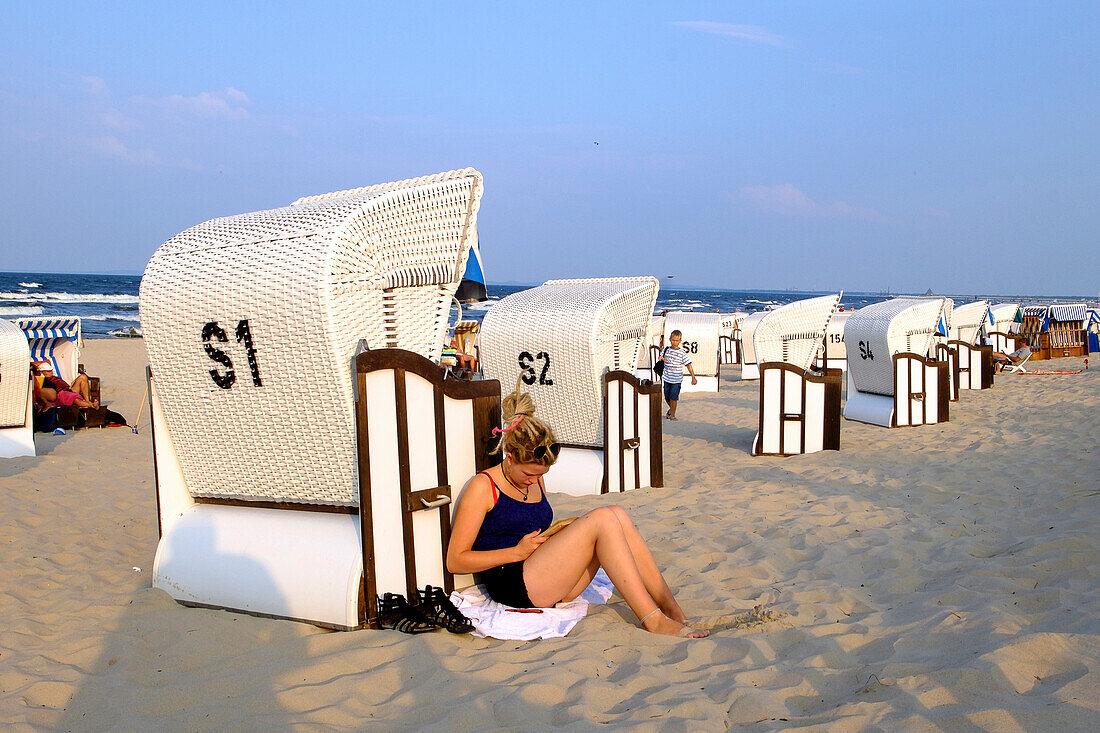 Young woman is leaning against a beach chair, reading a book, Strand, Bansin, Usedom, Ostseeküste, Mecklenburg-Vorpommern, Germany