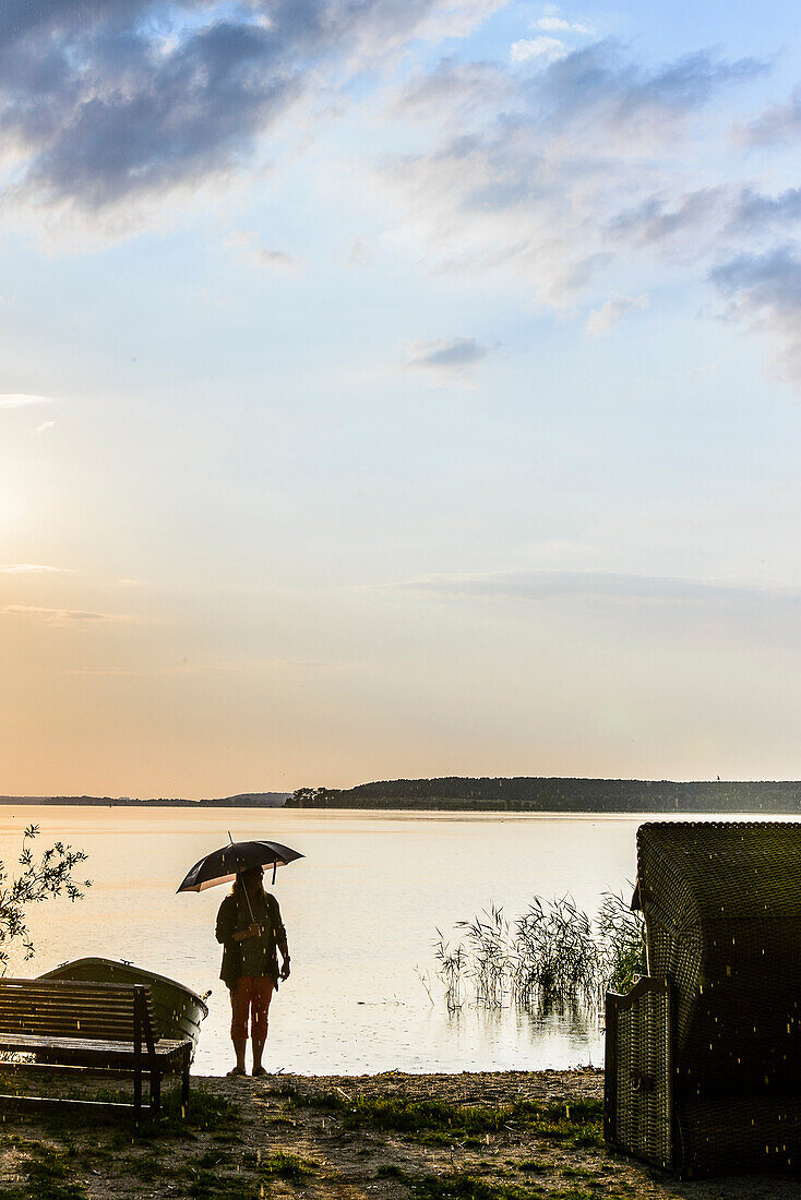 Woman standing with umbrella in backlight on the shore on the lagoon side in Lieper angle, Usedom, Baltic Sea coast, Mecklenburg-Vorpommern, Germany