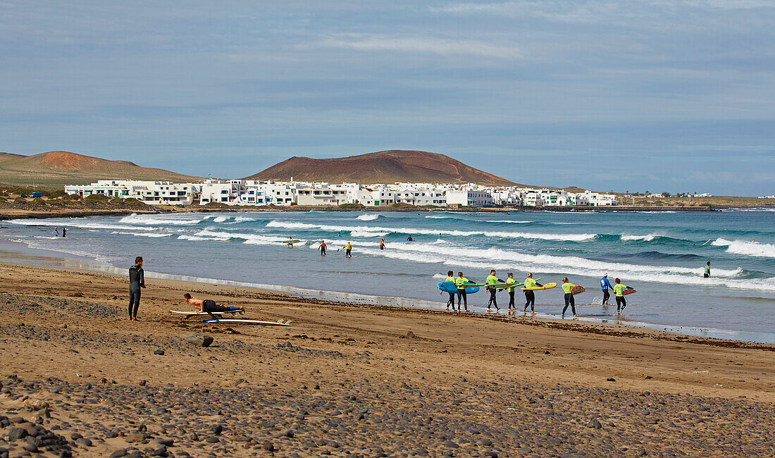 Surfer am Playa de Famara und die Ortschaft La Caleta de Famara, Atlantik, Lanzarote, Kanaren, Kanarische Inseln, Islas Canarias, Spanien, Europa