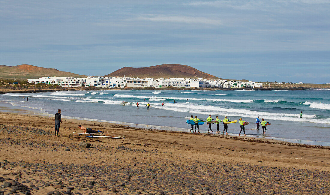 Surfer at the Playa de Famara and the village of La Caleta de Famara, Atlantic Ocean, Lanzarote, Canary Islands, Islas Canarias, Spain, Europe