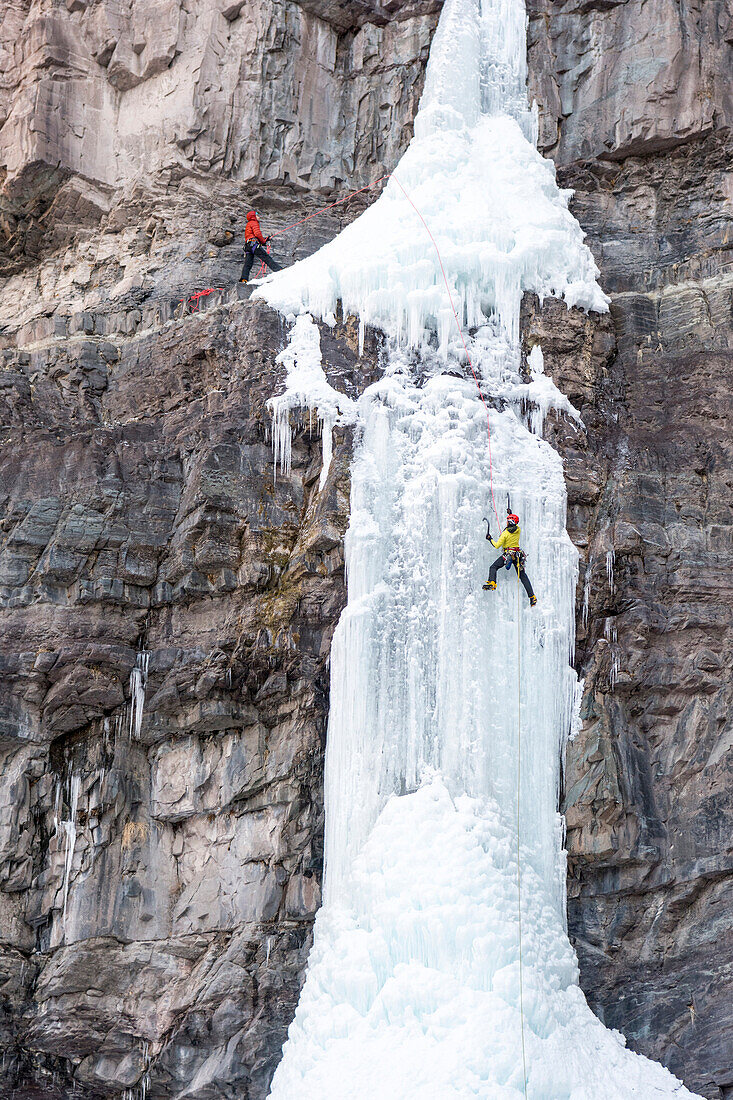 A man and woman ice climbing up a frozen waterfall called Cascade Falls in a basin right above the historic downtown of Ouray, Colorado, USA