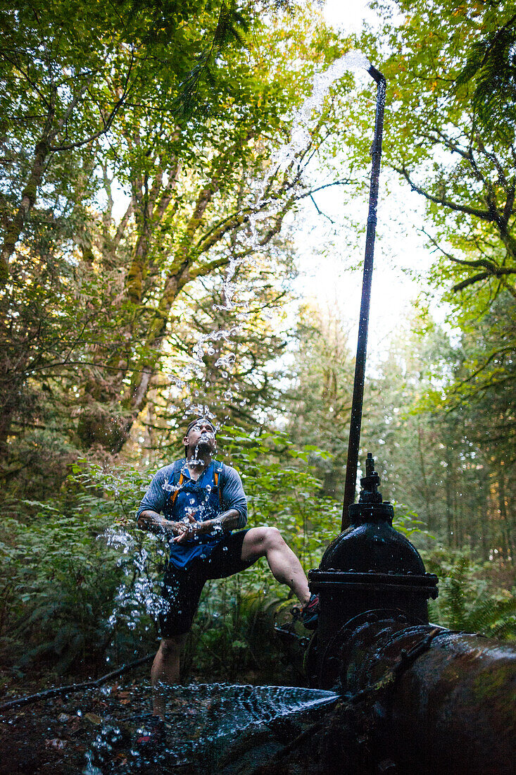 Man stops to drink water from fountain while trail running near Elbow Lake in Fraser Valley, Harrison Mills, British Columbia, Canada