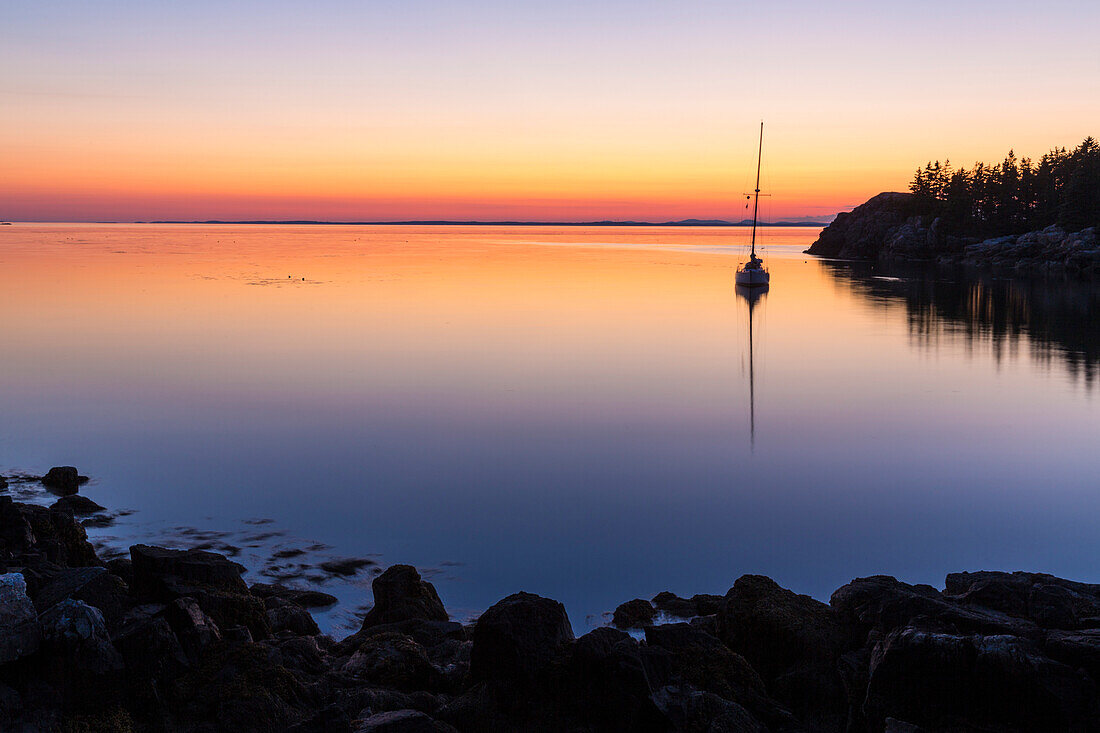 Silhouette of sailboat at sunset moored in Duck Harbor, Isle au Haut, Acadia National Park, Maine, USA