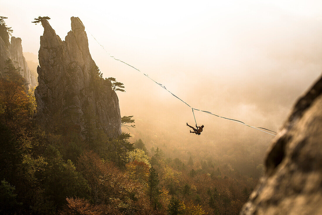 Silhouette of man hanging from highline high above foggy forest, Lower Austria, Austria
