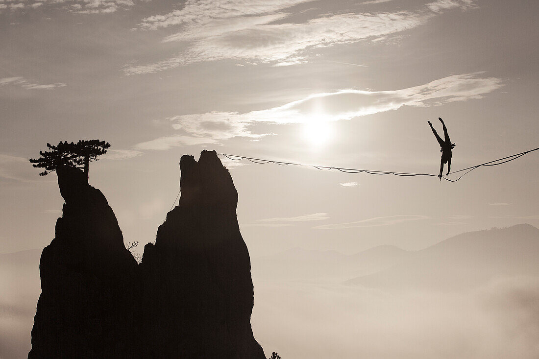 Silhouette of man doing handstand on highline against sun and over foggy hills, Lower Austria, Austria