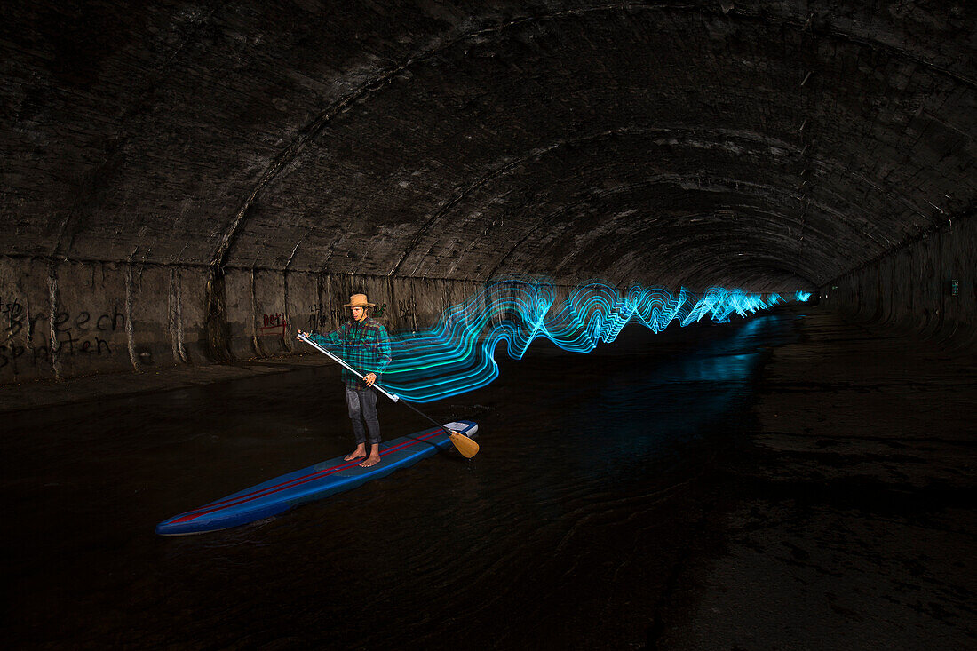 Man paddleboarding and light painting in underground river, Vienna, Austria