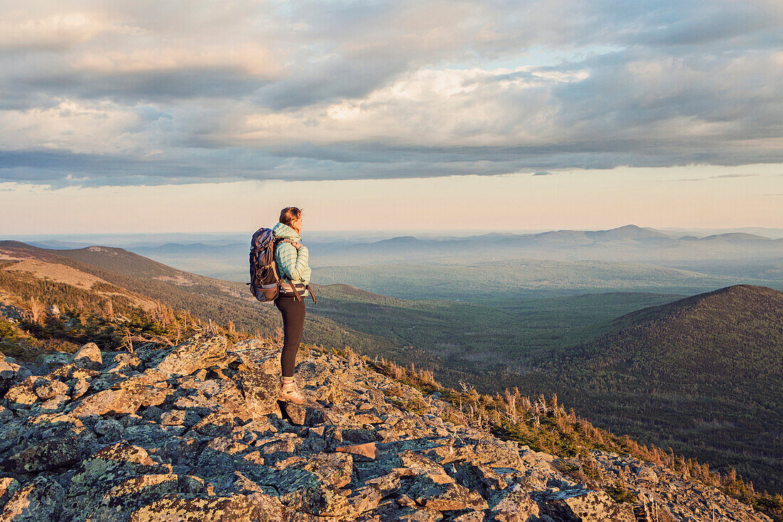 Female hiker standing and admiring landscape from top of Mount Abraham at dusk, Maine, USA