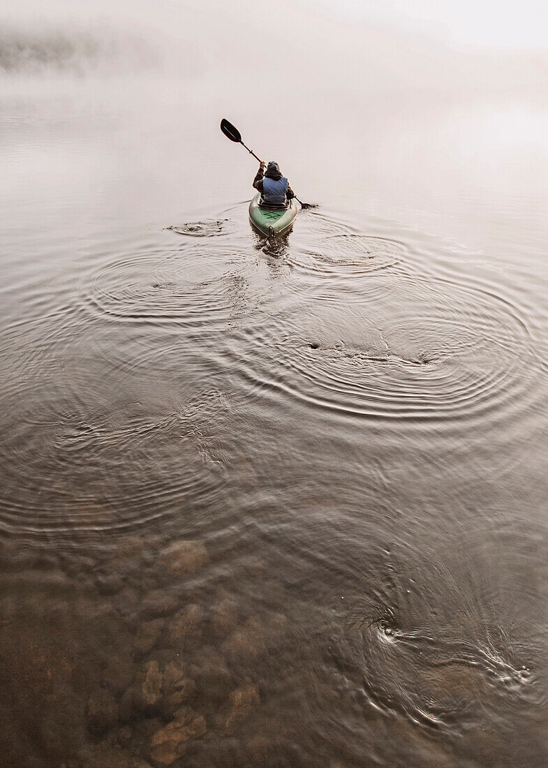 Young woman enjoys early morning paddle in kayak through mist on Daicey Pond in Maine's Baxter State Park, USA