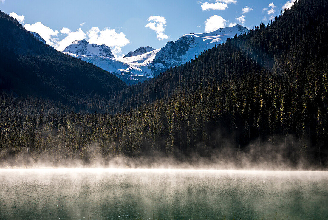 Fog rises off Lower Joffre Lake early in the morning and distant mountains can be seen covered in glaciers. This hike is a popular one with in the Duffy Lake Provincial Park due to its stunning views and ease of access. Pembreton, British Columbia, Canada