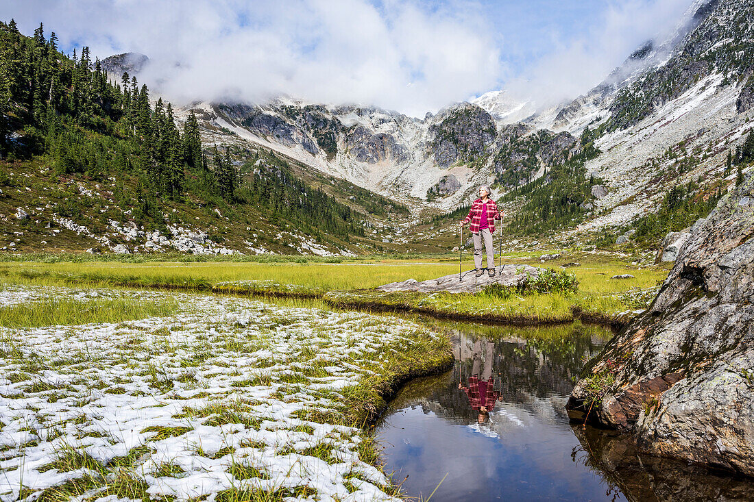A woman hikes through Brandywine Meadows, an alpine meadow very popular in the winter for backcountry snowmobiling, an a fall day and takes in the picturesque view of the surrounding mountains. Whistler, British Columbia, Canada