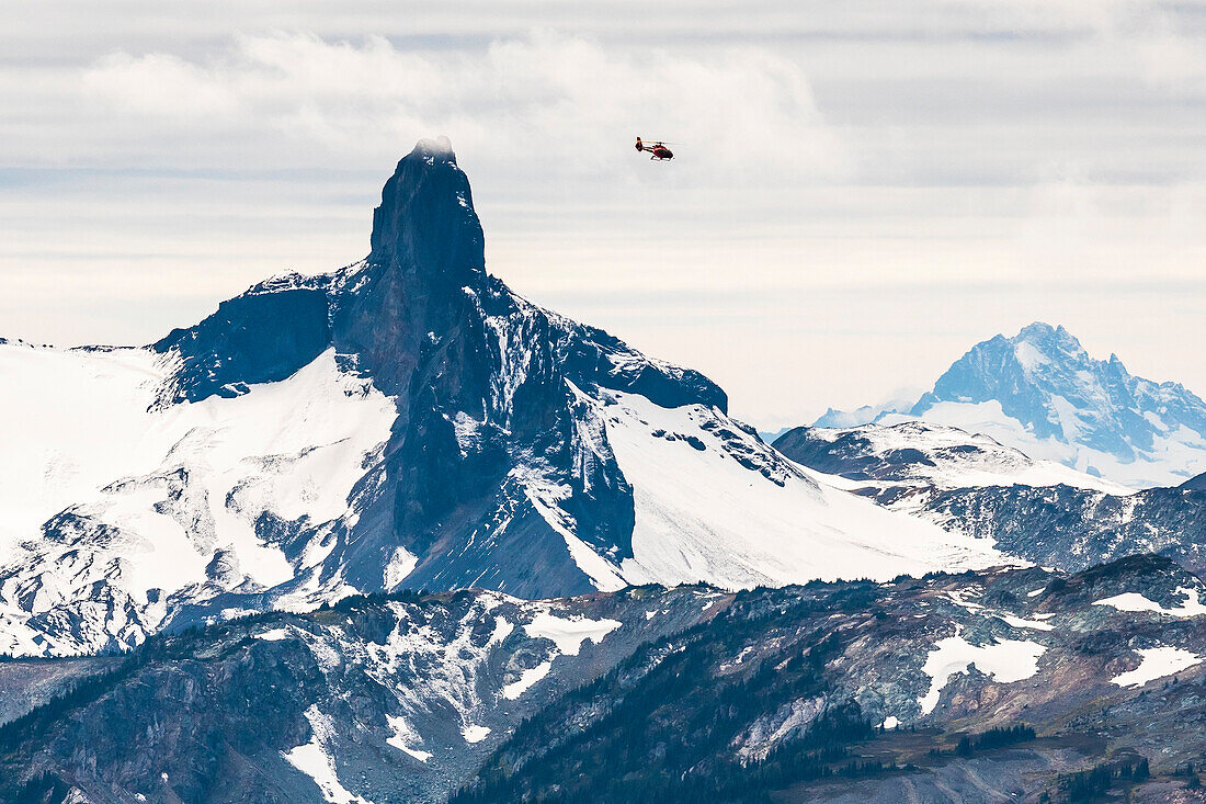 A helicopter flies by Black Tusk on a cloudy day in the alpine. Black Tusk is an iconic peak and easily recognizable from any direction in the Coast Mountains of British Columbia, Canada