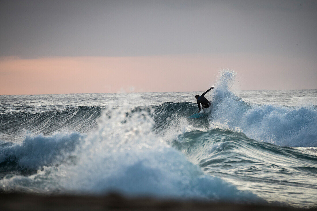 Surfer riding wave at sunset, Oahu, Hawaii, USA