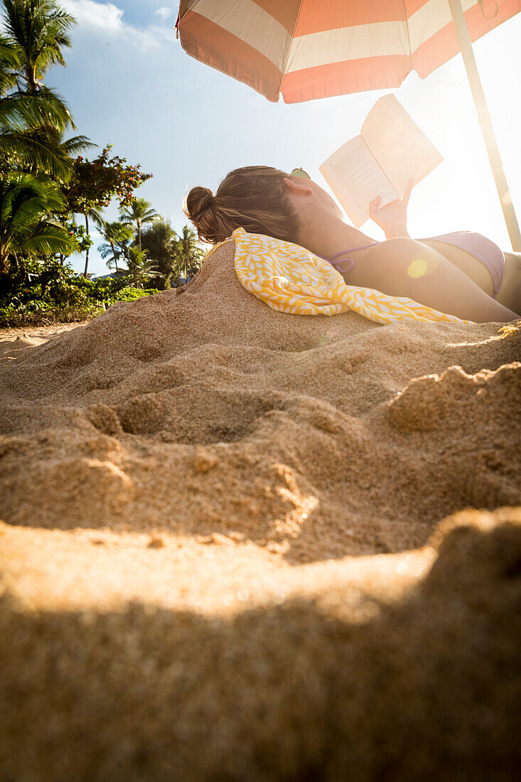 Woman in bikini reading book on beach, Oahu, Hawaii, USA