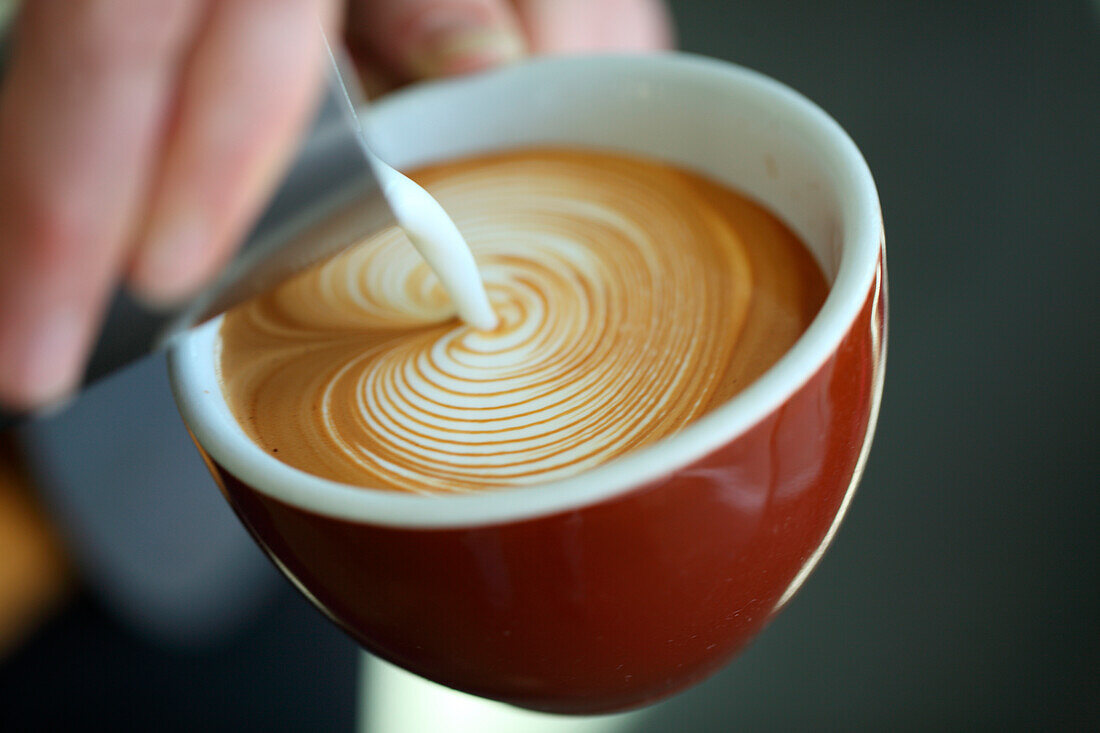 Close up of barista pouring milk into cappuccino, Oakland, California, USA