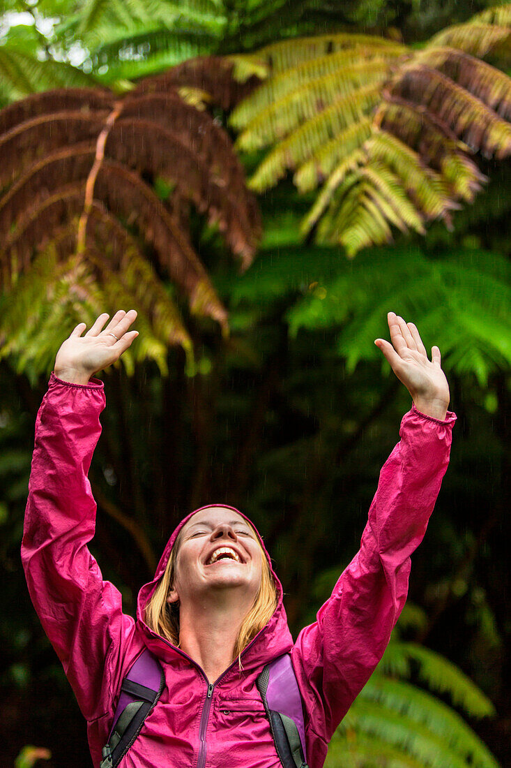 A woman raises her arms in joy during a light rain shower while hiking a forest near Volcano National Park on the Big Island of Hawaii.