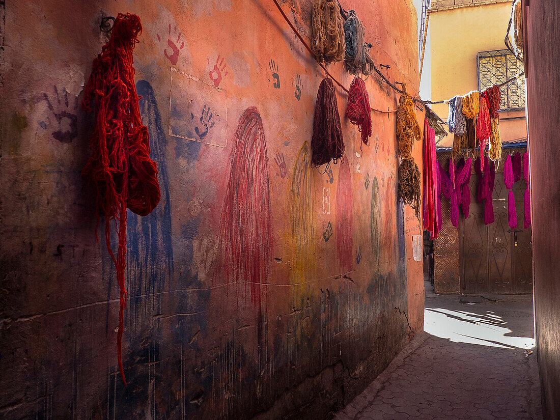 Colorful fabrics hanging in narrow alley decorated with handprints, Marrakesh, Morocco