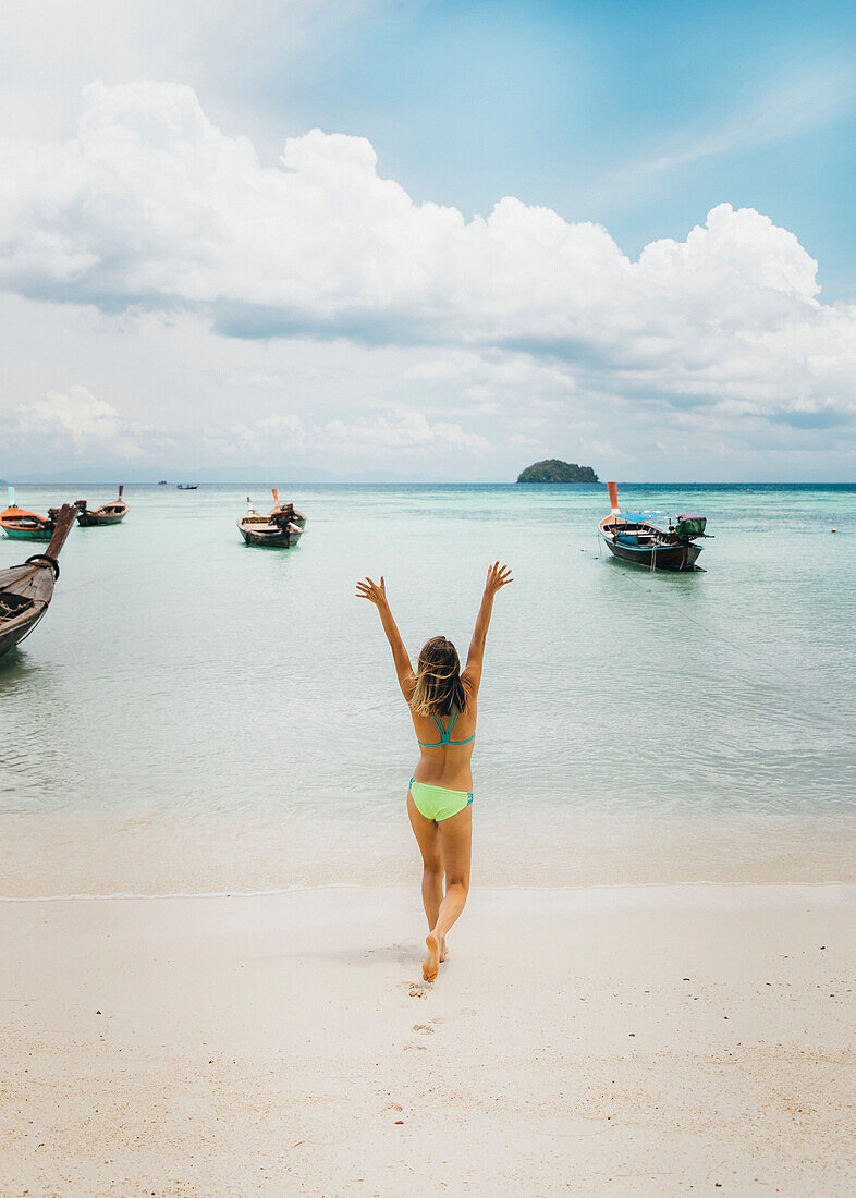 Young woman in bikini walking on beach towards sea with raised arms, Tambon Ko Tarutao, Chang Wat Satun, Thailand