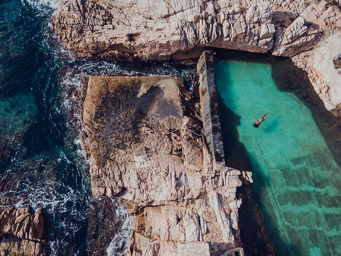 Aerial view of woman floating in pool on rocky seashore, Tenerife, Canary Islands, Spain
