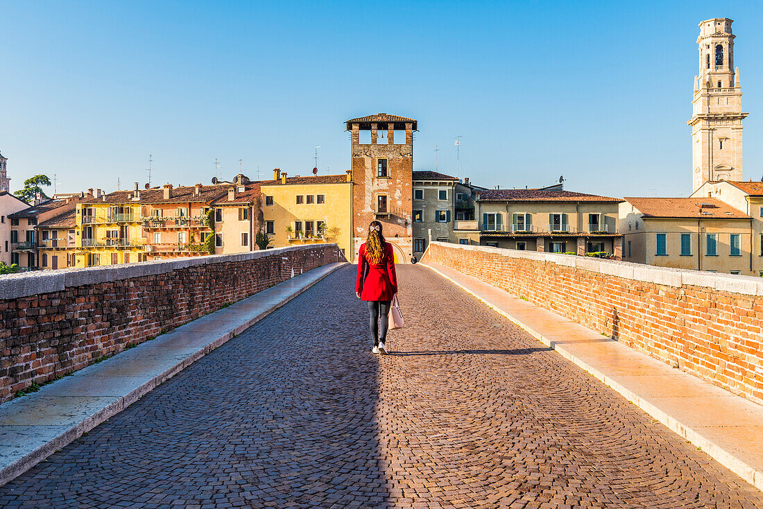Woman walking along the Ponte Pietra (Stone Bridge). Verona, Veneto, Italy