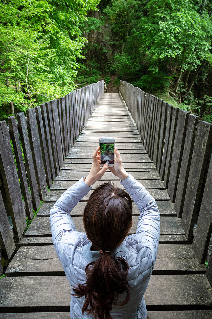A girl taking a picture on a wooden bridge on the trail of the Breggia gorges, Muggio Valley, Mendrisio District, Canton Ticino, Switzerland.